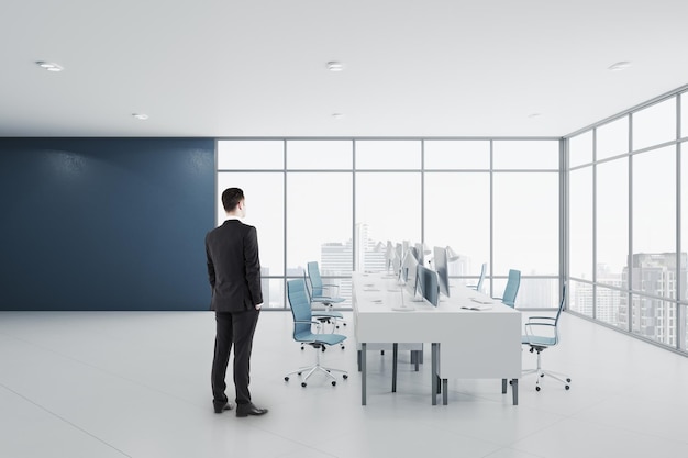 Homme d'affaires debout dans un intérieur de salle de bureau de coworking en béton moderne avec fenêtre panoramique avec vue sur la ville équipement lumière du jour et mobilier