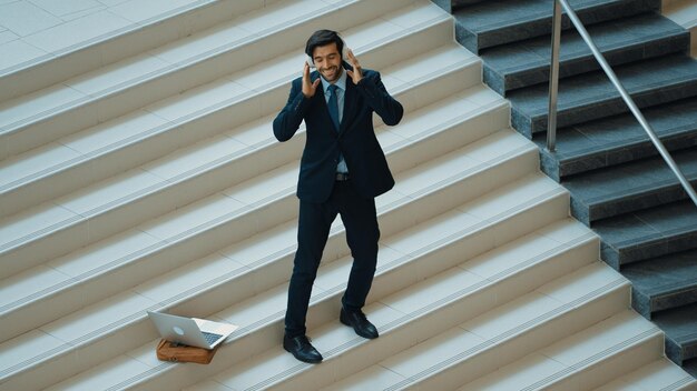 Photo homme d'affaires debout à l'escalier tout en se déplaçant à la musique de écouteurs exultant