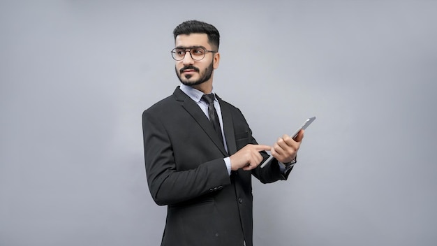 Homme d'affaires debout portant des lunettes posant sur fond gris en costume noir modèle pakistanais indien