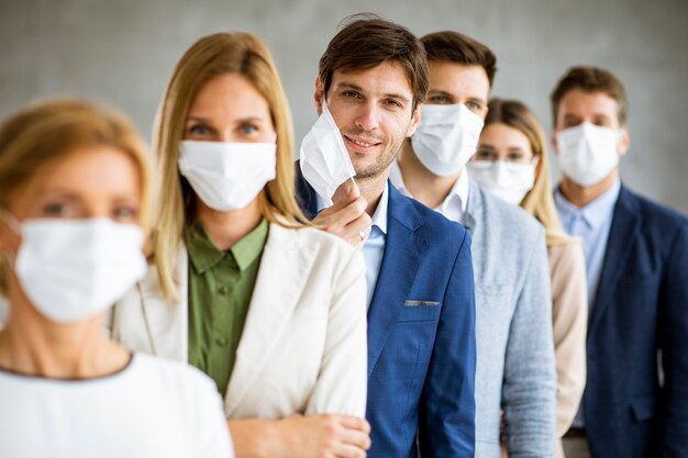 Homme d'affaires décollant son masque facial de protection et regardant la caméra avec les membres de l'histeam debout dans la ligne au bureau