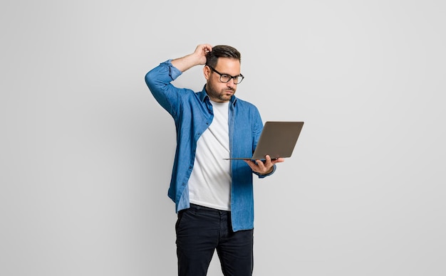 Homme d'affaires déçu confus avec la main dans les cheveux lisant un e-mail sur un ordinateur portable sur fond gris