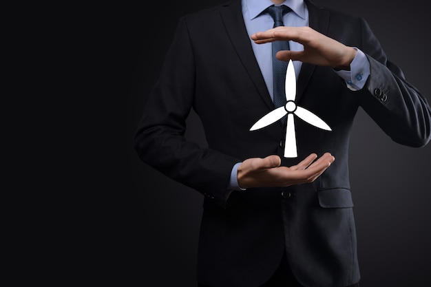 Homme d'affaires détenant une icône d'un moulin à vent qui produit de l'énergie environnementale. Fond sombre.