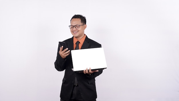 Homme d'affaires détient un ordinateur portable et regarde un téléphone portable isolé sur fond blanc