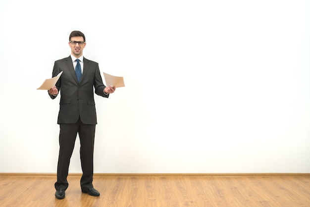 L'homme d'affaires détient des papiers sur le fond du mur blanc