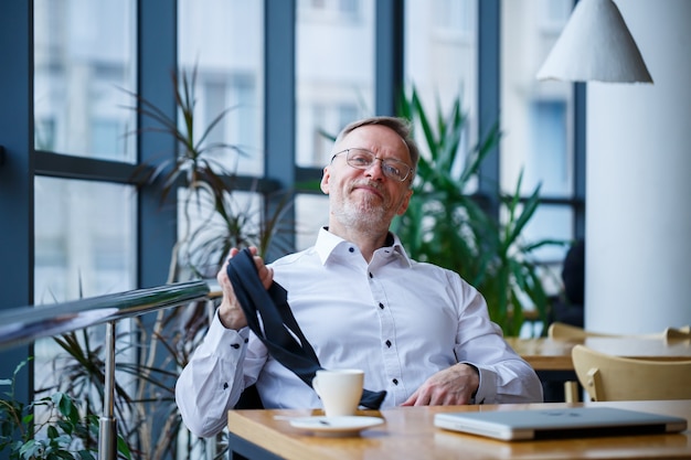 L'homme d'affaires directeur masculin adulte a travaillé avec succès et à la fin de la journée boit du café sans veste