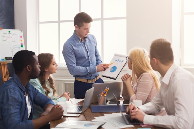 Homme d'affaires donnant une présentation à des collègues dans un bureau moderne. Équipe de jeunes entreprises discutant d'une nouvelle stratégie marketing, planifiant un projet de démarrage, espace de copie