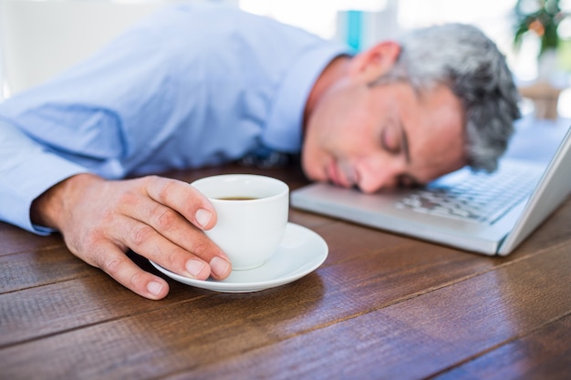 Homme d&#39;affaires, dormir sur ordinateur portable et toucher la tasse de café