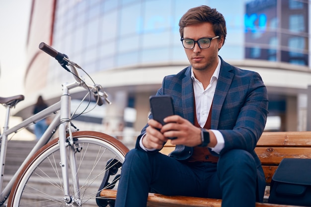 Homme d'affaires élégant à l'aide de smartphone près de vélo