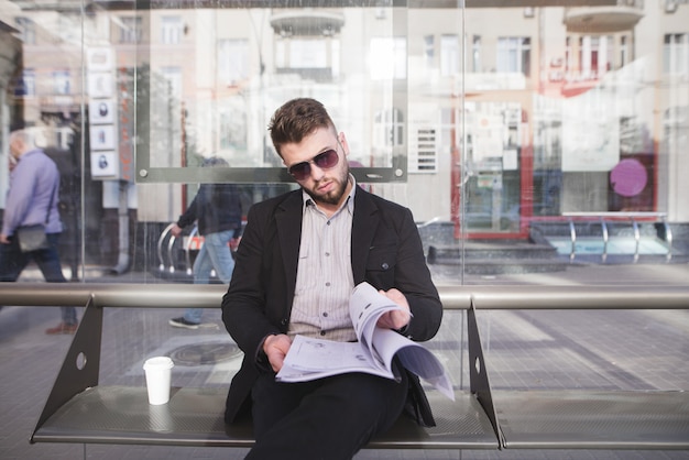 . Un homme d'affaires élégant dans ses lunettes et documents dans ses mains est assis sur le banc