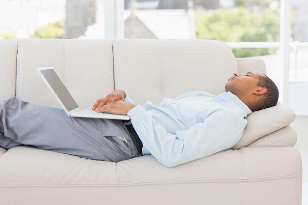 Homme d&#39;affaires endormi sur le canapé avec ordinateur portable
