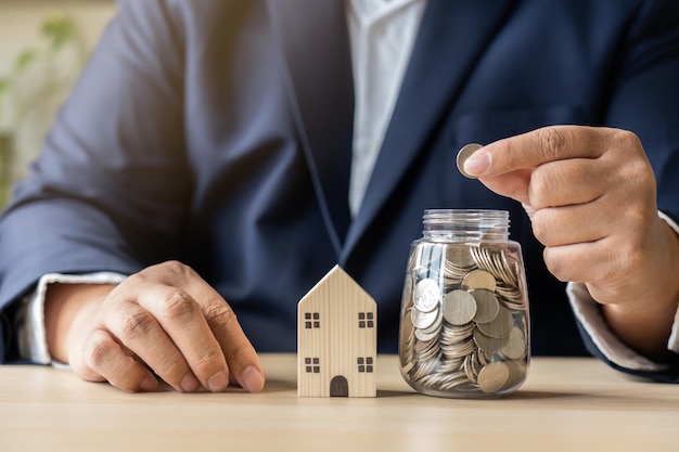 L'homme d'affaires épargne des pièces d'argent dans un bocal pour une nouvelle maison d'achat ou de location