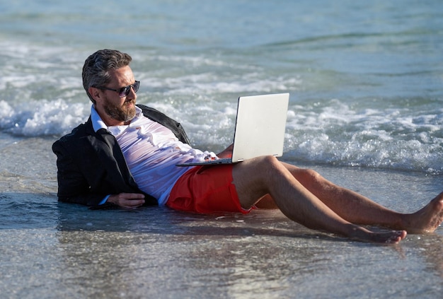 Homme d'affaires d'été se détendre à la plage Homme daffaires se détendre sur la plage homme d'affaires en costume avec ordinateur portable en été Homme d‘affaires rêve de l'été affaires en mer se recharger à travers les voyages