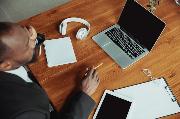 Homme d'affaires ou étudiant travaillant à domicile isolé ou maintenu en quarantaine à cause du coronavirus. Homme afro-américain utilisant un ordinateur portable, une tablette et un casque. Conférence en ligne, cours, bureau à distance.