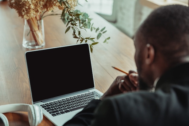 Homme d'affaires ou étudiant travaillant à domicile isolé ou maintenu en quarantaine à cause du coronavirus. Homme afro-américain utilisant un ordinateur portable, une tablette et un casque. Conférence en ligne, cours, bureau à distance.