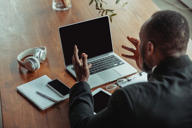 Homme d'affaires ou étudiant travaillant à domicile isolé ou maintenu en quarantaine à cause du coronavirus. Homme afro-américain utilisant un ordinateur portable, une tablette et un casque. Conférence en ligne, cours, bureau à distance.