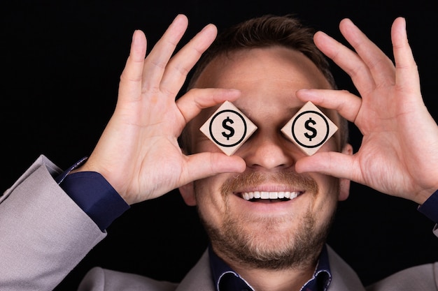 Un homme d'affaires exprime des émotions avec ses mains et son visage avec des blocs de bois et des signes de dollars américains.