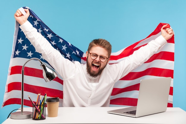 Photo homme d'affaires extrêmement heureux levant le drapeau américain, criant une joie folle sur le lieu de travail, célébrant la fête du travail ou le jour de l'indépendance des états-unis le 4 juillet, aide gouvernementale à l'emploi. d'intérieur, isolé