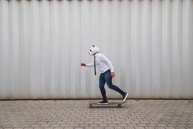 Homme d'affaires faisant de la planche à roulettes sur un longboard avec un masque d'ours panda contre un mur gris