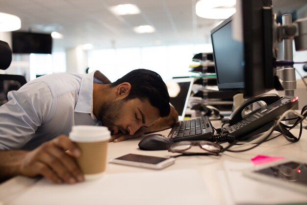 Homme d'affaires fatigué de dormir par des ordinateurs de bureau au bureau