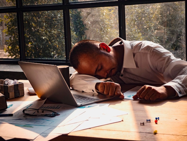 Photo un homme d'affaires fatigué qui dort devant un ordinateur portable et des papiers sur la table.