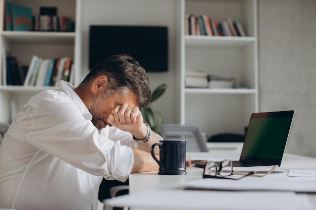 Homme d'affaires fatigué s'endormant pendant le travail avec des documents et un ordinateur portable au bureauxA