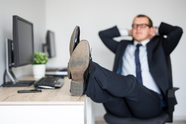 Homme d'affaires fatigué se relaxant dans un bureau moderne assis avec les jambes sur la table