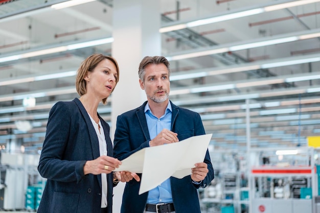 Homme d'affaires et femme d'affaires discutant du plan dans un hall d'usine