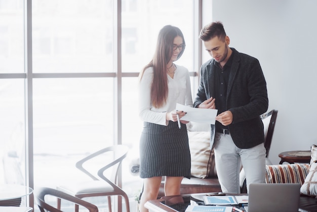 Homme d'affaires et femme d'affaires étudiant un graphique sur la plaque et les documents papier à la fenêtre sur le bureau de la ville à un étage élevé