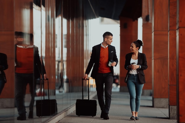 Homme d'affaires et femme d'affaires parlant et tenant des bagages voyageant en voyage d'affaires, transportant du café frais dans leurs mains. Notion d'entreprise. Photo de haute qualité