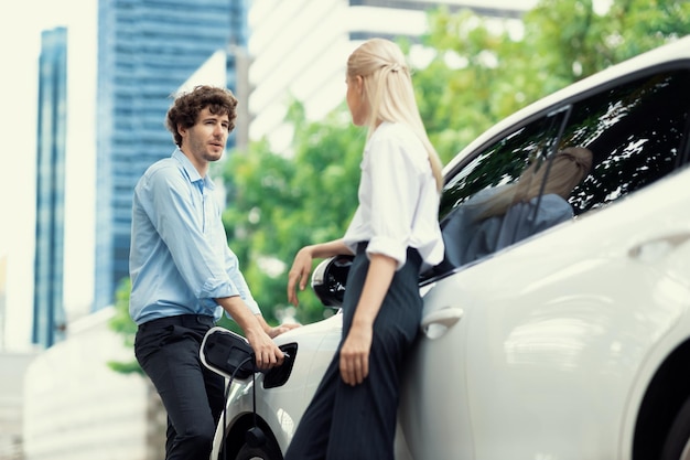 Homme d'affaires et femme d'affaires progressiste avec voiture EV et station de recharge