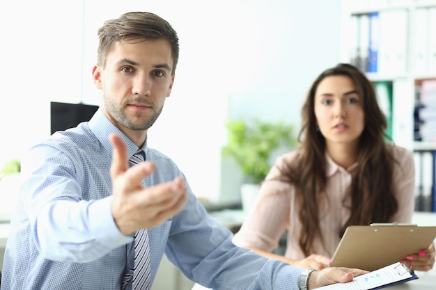 Homme d'affaires avec femme étend ses mains vers l'avant assis au bureau