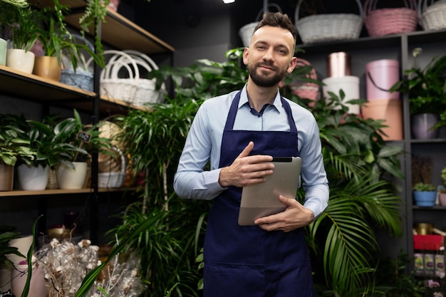 Homme d'affaires fleuriste entouré de plantes en pot dans sa boutique tenant une tablette dans ses mains à la recherche