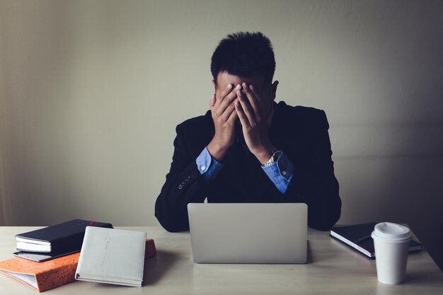 Un homme d'affaires frustré couvrant le visage alors qu'il est assis sur la table