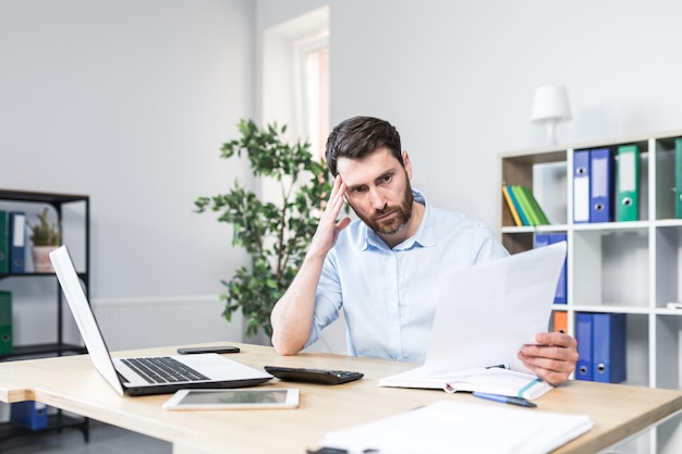 Un homme d'affaires frustré et inquiet examine les mauvaises performances de l'entreprise sur les documents qu'un homme diabolique tient entre ses mains des rapports financiers avec des erreurs