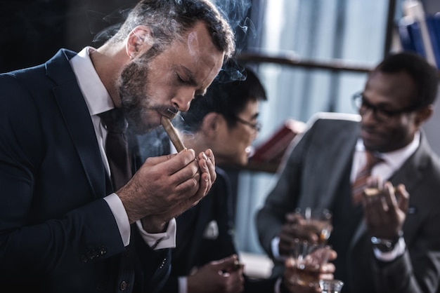 Homme d'affaires fumant un cigare avec une équipe commerciale multiculturelle passant du temps derrière