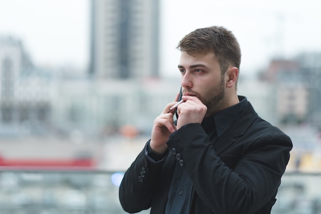 Un homme d'affaires fume une cigarette et parle par téléphone sur un paysage de la ville.