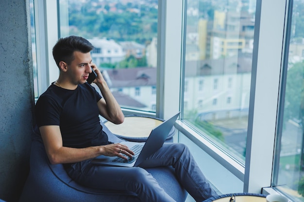 Homme d'affaires gai parlant au téléphone travaillant avec un ordinateur portable au bureau Un homme d'affaires est assis et travaille sur un ordinateur portable