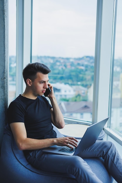 Homme d'affaires gai parlant au téléphone travaillant avec un ordinateur portable au bureau Un homme d'affaires est assis et travaille sur un ordinateur portable