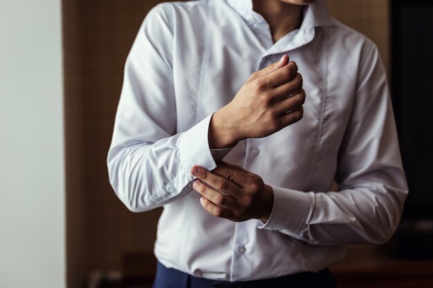 Homme d'affaires habille chemise blanche, gros plan mains mâles, marié se prépare le matin avant la cérémonie de mariage,