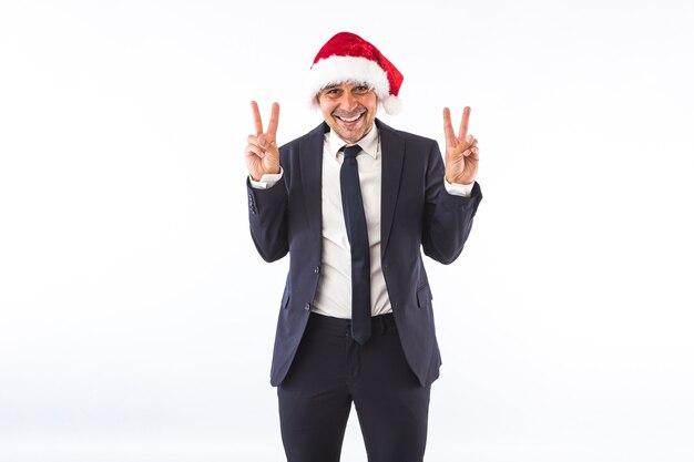 Homme d'affaires habillé en costume, cravate et chapeau de Noël du Père Noël, s'amusant, sur fond blanc. Notion de célébration de Noël.