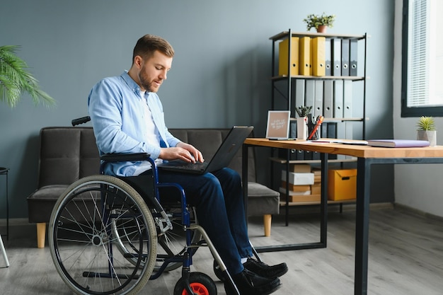 Homme d'affaires handicapé assis dans un fauteuil roulant à l'aide d'un ordinateur sur le lieu de travail