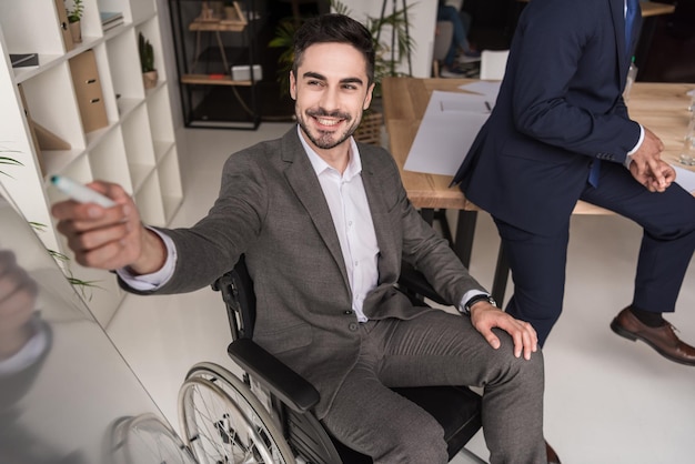 Homme d'affaires handicapé souriant en fauteuil roulant pointant vers le tableau blanc lors d'une réunion d'affaires avec