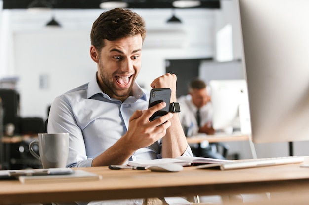 Homme d'affaires heureux choqué à l'aide de smartphone et se réjouit alors qu'il était assis près de la table au café