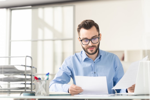 Homme d'affaires heureux et confiant avec des papiers préparant un rapport ou lisant les termes du contrat avant la négociation