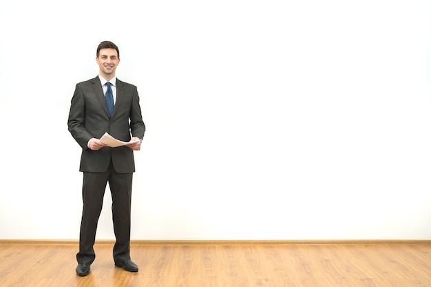 L'homme d'affaires heureux détient des papiers sur le fond du mur blanc