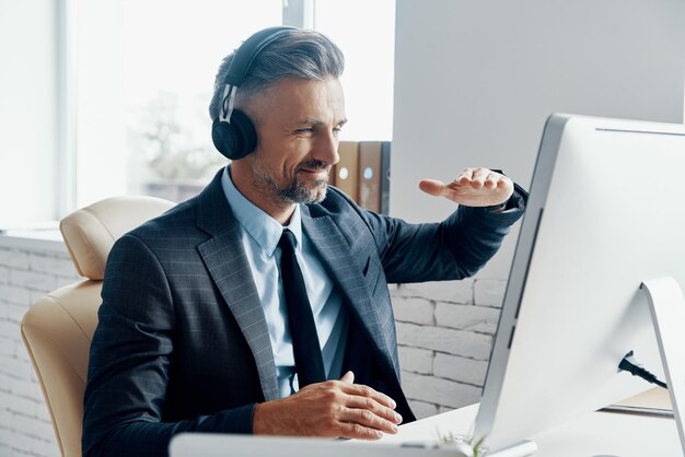 Un homme d'affaires heureux avec des écouteurs en train de tenir une conférence sur le web alors qu'il est assis à son lieu de travail