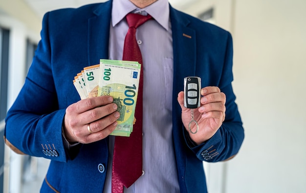Homme d'affaires heureux tenant des clés de voiture avec de l'argent en euros dans le concept de finance de bureau