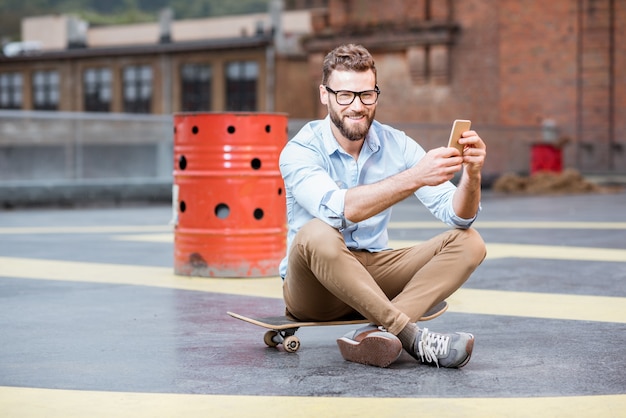 Homme d'affaires hipster assis avec un téléphone intelligent sur le terrain de jeu sur le toit du bâtiment industriel. Concept d'entreprise de style de vie