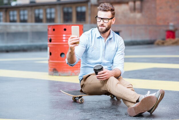 Homme d'affaires hipster assis avec un téléphone intelligent sur le terrain de jeu sur le toit du bâtiment industriel. Concept d'entreprise de style de vie