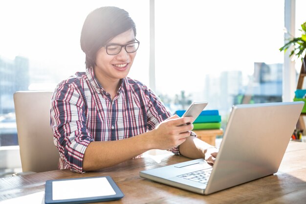 Homme d&#39;affaires hipster souriant à l&#39;aide de smartphone au bureau